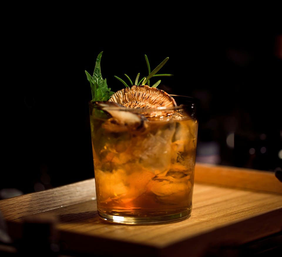 Amber cocktail with ice, garnished with herbs and dried citrus.
